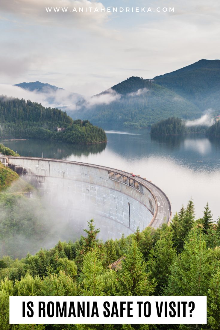 Morning mist surrounds Vidraru Dam and forested hills in Romania, with Pinterest overlay: “Is Romania Safe to Visit?”