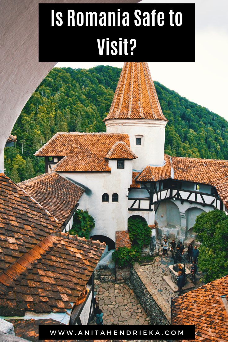 A view into the courtyard of Bran Castle in Romania, framed by red rooftops and green forest, with overlay text: “Is Romania Safe to Visit?”