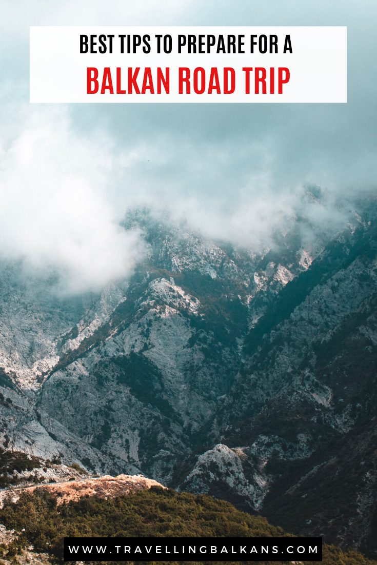 A dramatic mountain range partially covered in mist with jagged peaks and rugged terrain. Overlay text reads “Best Tips to Prepare for a Balkan Road Trip,” with the URL “www.travellingbalkans.com” displayed at the bottom.