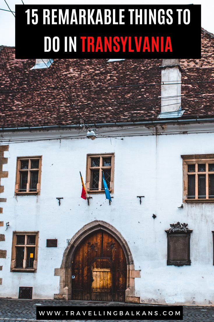 Historic white building with flags and arched wooden door in Transylvania, Romania, with text overlay: “15 Remarkable Things to Do in Transylvania.”