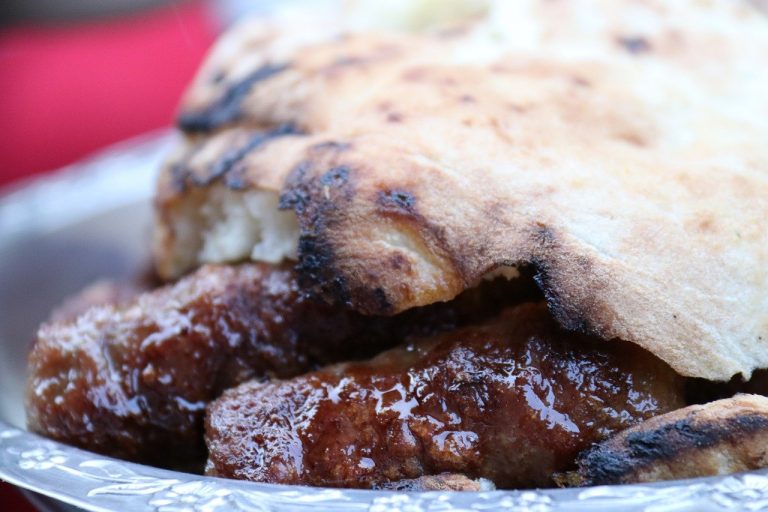 Close-up of juicy grilled ćevapi sausages served in a charred, folded flatbread, a classic Balkan street food.